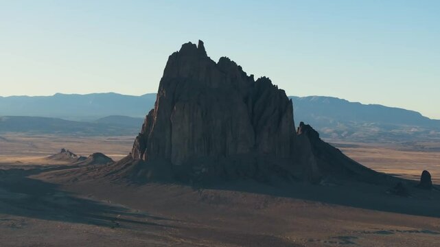 A breathtaking, slow-rotating 70mm aerial shot of the sacred &ldquo;Ship Rock&rdquo;, a massive, monolithic rock butte, towering above the high desert plain of the Navajo Nation, in New Mexico, during sunset.