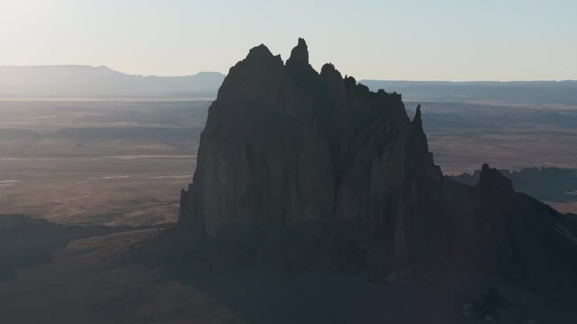 An unworldly, high-contrasted aerial shot of the sacred &ldquo;Ship Rock&rdquo;, a massive, monolithic rock butte, towering above the high desert plain of the Navajo Nation, in New Mexico, as the sun sets behind.
