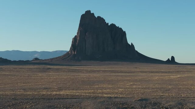A low to the ground, slow-rising 70mm drone shot of the sacred &ldquo;Ship Rock&rdquo;, a massive, monolithic monadnock towering above the high-desert plain of the Navajo Nation, in New Mexico, United States.