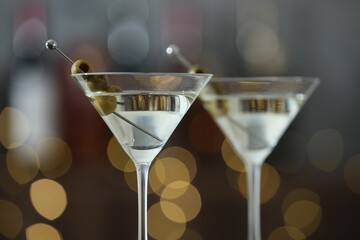 Martini cocktail with olives in glasses on blurred background, closeup. Bokeh effect