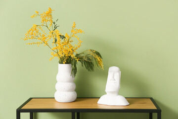 Vase with mimosa flowers and decor on shelf near green wall