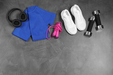 Stylish sportswear, white sneakers, dumbbells, skipping rope and headphones on grey background, flat lay. Space for text
