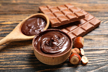 Bowl and spoon of sweet chocolate spread with hazelnuts on wooden background