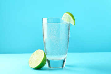 Soda water with lime in glass on light blue background