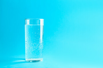 Soda water in glass on light blue background, space for text