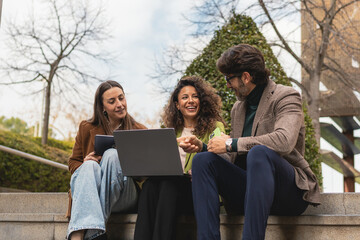 Business Team Collaborating on Laptop Outdoors. Three professionals sitting on outdoor steps, discussing work on a laptop, showcasing teamwork, collaboration, and productivity.