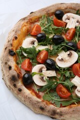 Tasty pizza with cherry tomatoes, black olives, mushrooms and arugula on white table, closeup