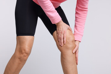 Woman suffering from pain in her knee on light grey background, closeup