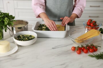 Woman making spinach lasagna at marble table indoors, closeup