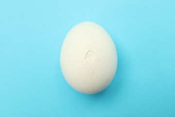 One egg with cracked shell on light blue background, top view