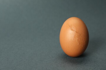 One egg with cracked shell on grey background, closeup. Space for text