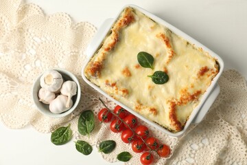 Delicious spinach lasagna in baking dish and ingredients on white table, flat lay