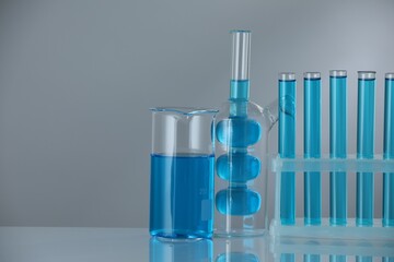 Laboratory glassware with blue liquid on mirror surface against grey background. Space for text