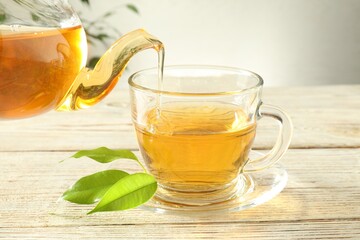 Pouring freshly brewed tea from teapot into glass cup on wooden table, closeup