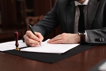 Notary signing document at table in office, closeup