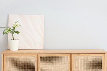 Houseplant with painting on stylish wooden chest of drawers near white wall in room