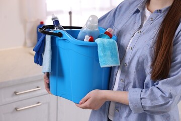 Woman holding bucket with cleaning supplies in kitchen, closeup