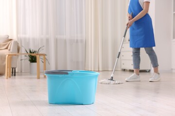 Woman cleaning floor with string mop indoors, focus on bucket © New Africa