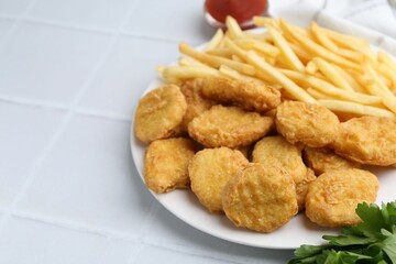 Tasty chicken nuggets and french fries on white tiled table. Space for text