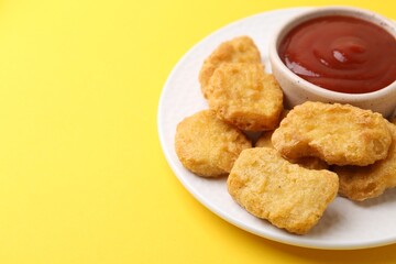Tasty chicken nuggets with sauce on yellow background, closeup. Space for text