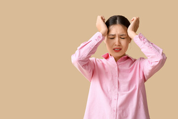 Young Asian woman suffering from headache on beige background. Brain Injury Awareness Month