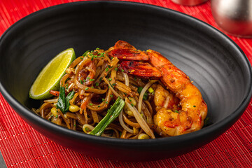 Top view of shrimp Pad Thai with lime in a black bowl