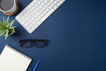 Workspace with keyboard, laptop, office supplies, pen, green leaf and coffee cup. Flat lay, top view blue office desk