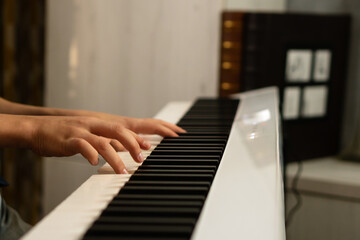 Fototapeta premium Close-up of a boy's hands playing a white digital piano. Practicing piano at home. The concept of education