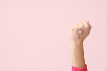 Raised woman's fist with drawn female symbol on pink background. Women's history month