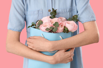 Young woman with gift bag of ranunculus flowers and eucalyptus on pink background, closeup