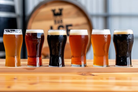 Five glasses of varied craft beers on wooden table in brewery setting