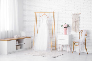 Vase with bouquet of beautiful ranunculus flowers near wedding dress on hanger at home