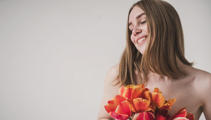 Red-haired girl, natural beauty with a bouquet of tulips on a light background, minimalism,...