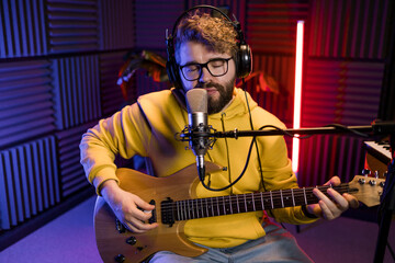 Man vocal artist singing in a recording studio with guitar. Male singer singing a song and playing guitar. Sound record and music streaming concept