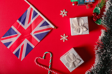 A festive flat lay featuring a Union Jack flag, two white gift boxes with bows, snowflakes, holly...