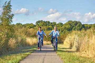 mature cheerful couple holding hands while riding a bike in spring season