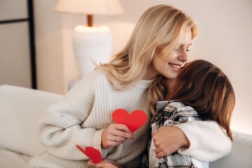 Celebrating, with paper hearts. Mother and daughter are together in domestic room