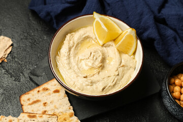 Bowl of delicious hummus with lemon and crispbreads on black grunge background