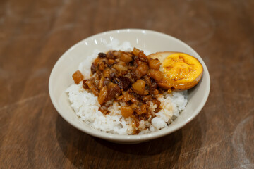 Taiwanese braised pork rice with a hard-boiled egg in a bowl on a wooden table.