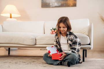 Obraz premium Gift box in hands, birthday. Cute little girl is in the domestic room alone