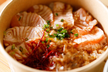 Donburi with sliced salmon on sushi rice in paper container. Healthy take away food.