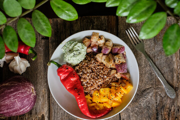 Bowl with buckwheat, fried eggplant cubes, yellow tomatoes, hot pepper and green sauce.