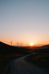Naklejka premium Winding road to wind turbines at sunset