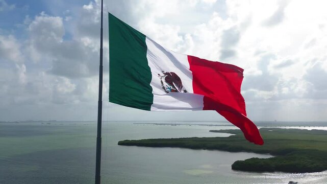 Mexican flag flying on a flagpole in the median of the Cancun Quintana Roo hotel zone, beautiful waves, sea and beach are seen in the background, as well as the Nichupté lagoon on a beautiful day