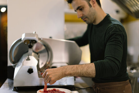 Man slicing cured meat with deli slicer