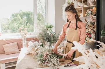 girl florist makes bouquet surrounded by fresh flowers in shop. Copyspace. Spring bloom