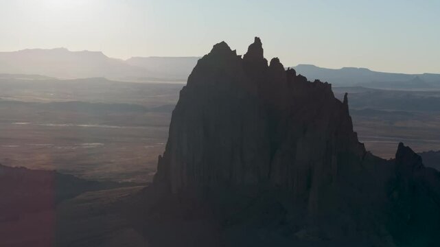 An unworldly, high-contrasted aerial shot of the sacred &ldquo;Ship Rock&rdquo;, a massive, monolithic rock butte, towering above the high desert plain of the Navajo Nation, in New Mexico, as the sun sets behind.