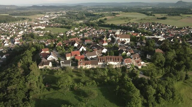 Drone footage moving forward from the opposite side, focusing on the historic town of Aach and its church tower, with a beautiful view of the surrounding landscape.