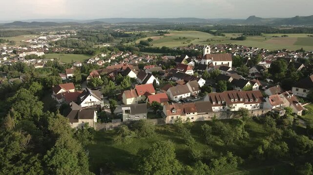 Drone footage orbiting leftwards around Aach village, focusing on the church tower and the historic town, while showcasing the surrounding landscape and village life.