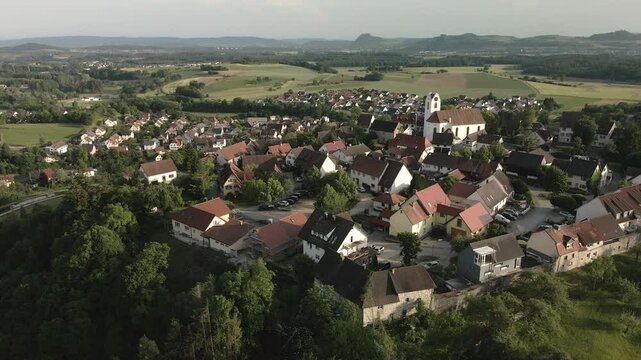 Drone footage orbits leftwards around Aach village from a new angle, highlighting the church tower and the charming old town against the scenic backdrop.